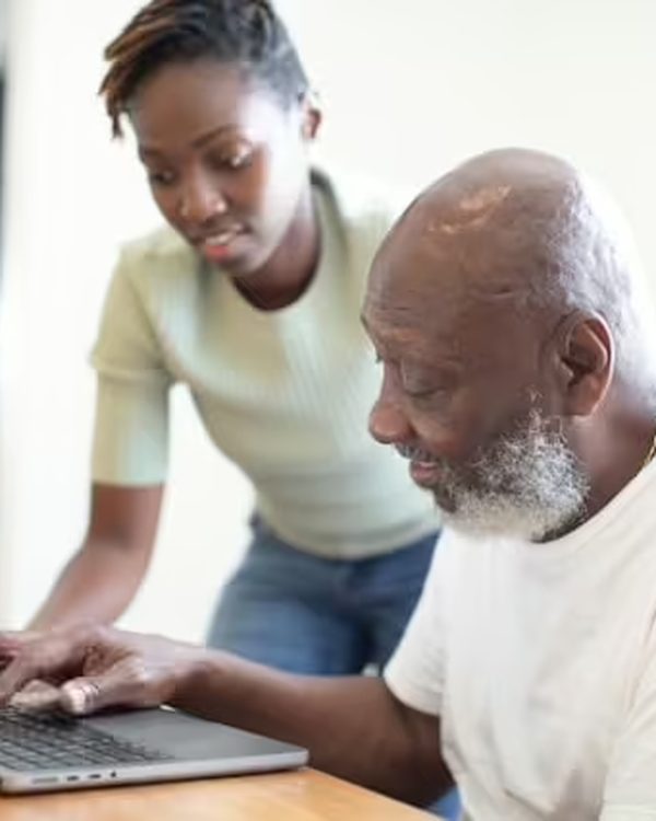A young woman helping an older man use a laptop