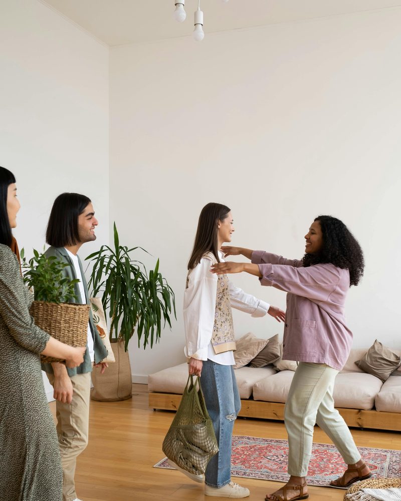 A small group warmly greeting each other in a living room, one carrying a potted plant