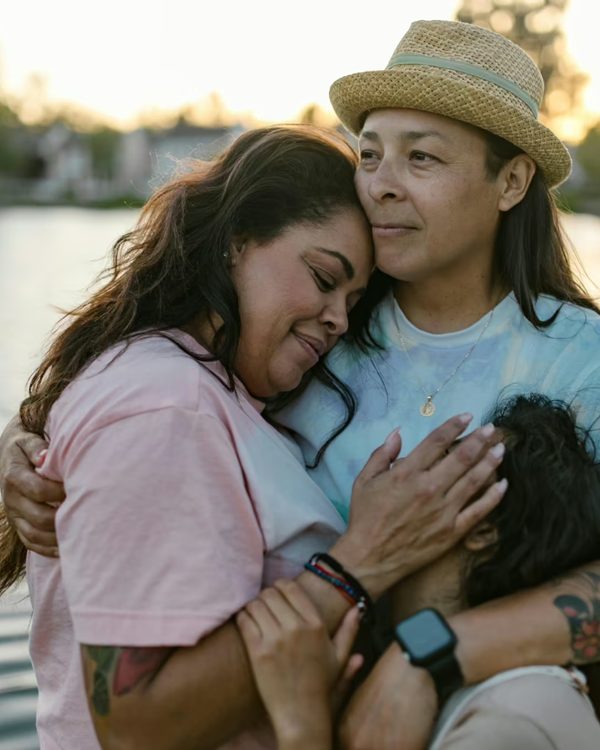 Two women holding each other outdoors near water
